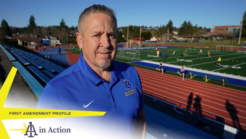Joe Kennedy, wearing a blue polo. stands in front of a track and football field. The 1A in Action logo overlays the image